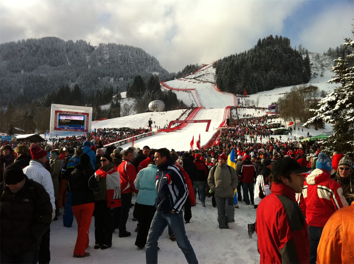 Menschen im Zielgelände am Hahnenkamm, dahinter die Streif im Schnee